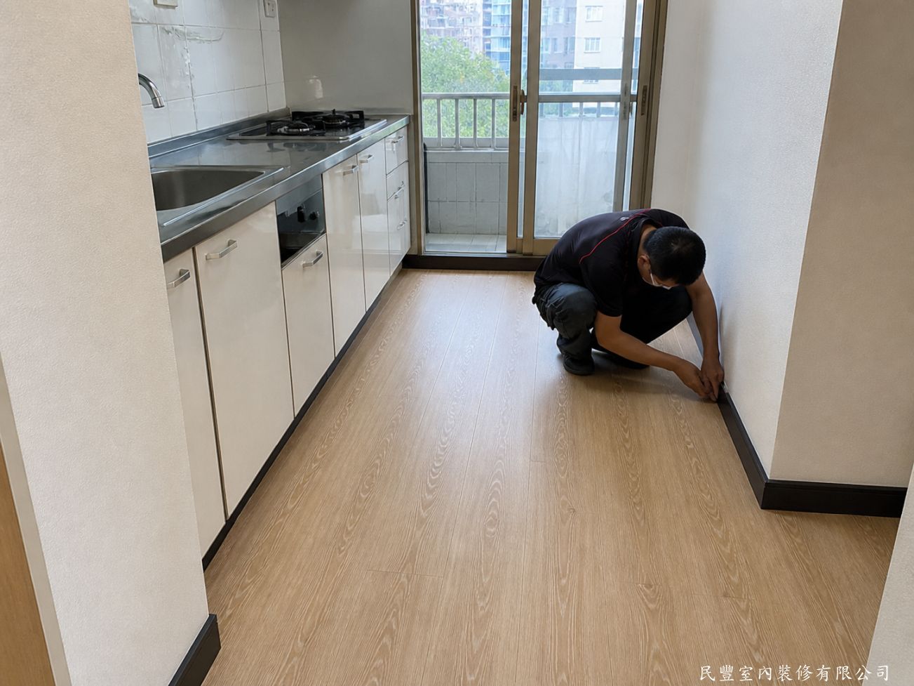 民豐室內裝修-超耐磨木地板浮鋪翻新-廚房區域同步鋪設超耐磨木地板，師傅在廚具旁進行最後收邊施作，確保廚房與客廳地板無縫銜接，整體一致美觀